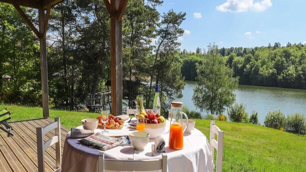Een tafel buiten gedekt met ontbijtartikelen, een krant en uitzicht op een meer.