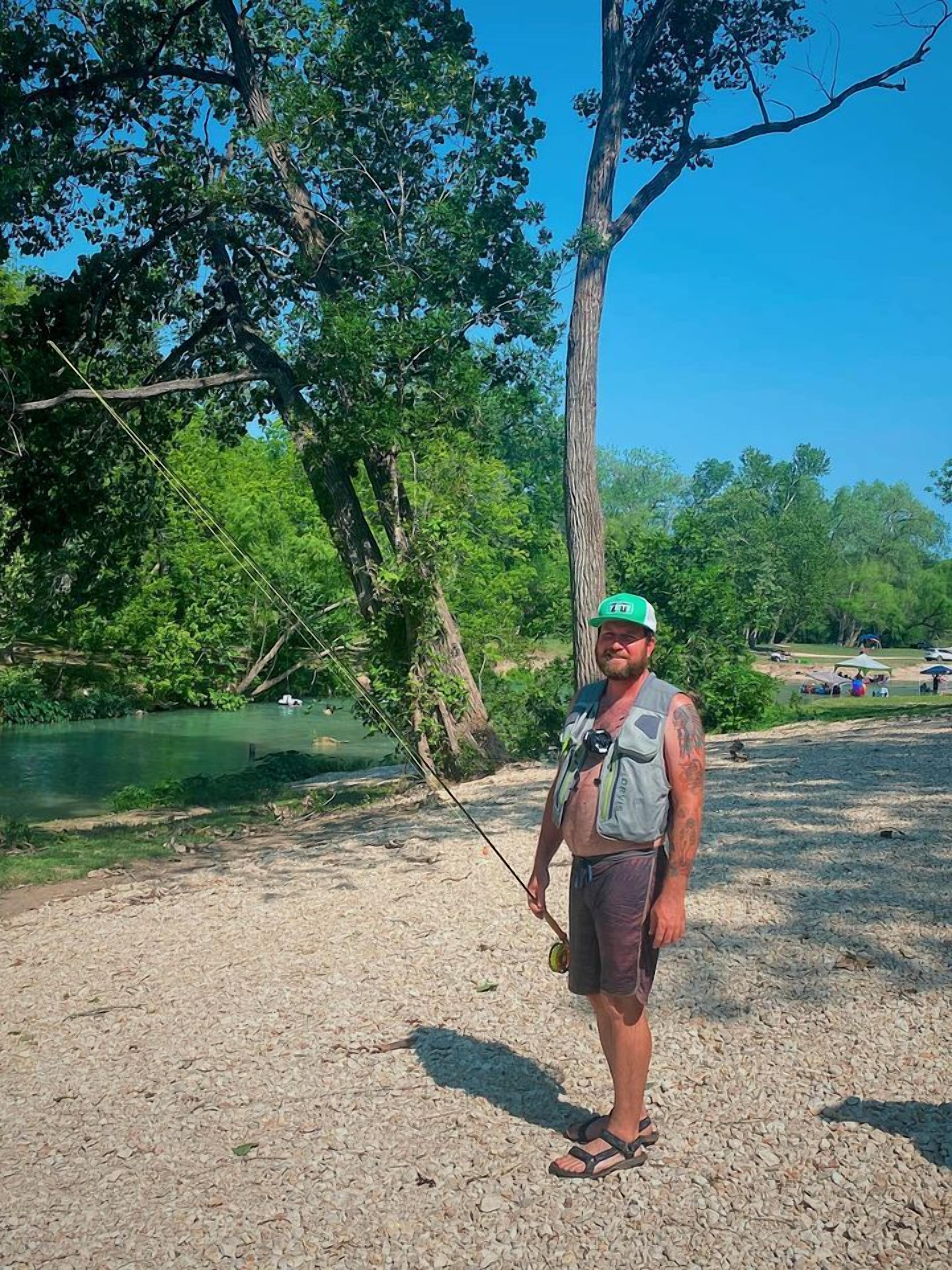 A person standing outdoors near a body of water, holding a fishing rod.
