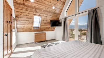 A bedroom with a wooden ceiling, a bed, a dresser, a TV, and a balcony with a view.