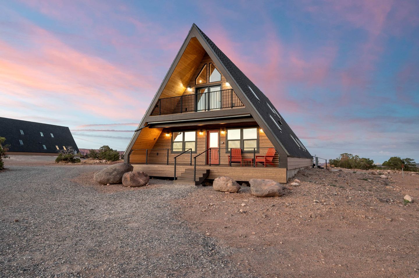 A modern, triangular-shaped cabin with a wooden exterior, a balcony, and a gravel driveway.