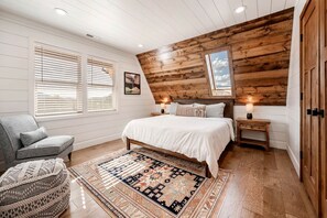 A bedroom with a wooden ceiling, a bed with white bedding, a patterned rug, a chair, and a nightstand with a lamp. - Gorgeous A-frame Settled in the Middle of the Desert inTorrey, Utah (Torrey)