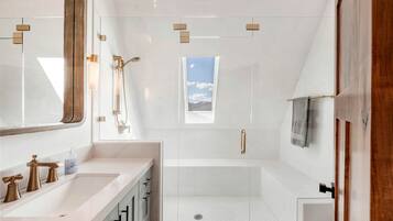 Un bagno moderno con doccia vetrata, uno specchio grande e una finestra vista cielo.