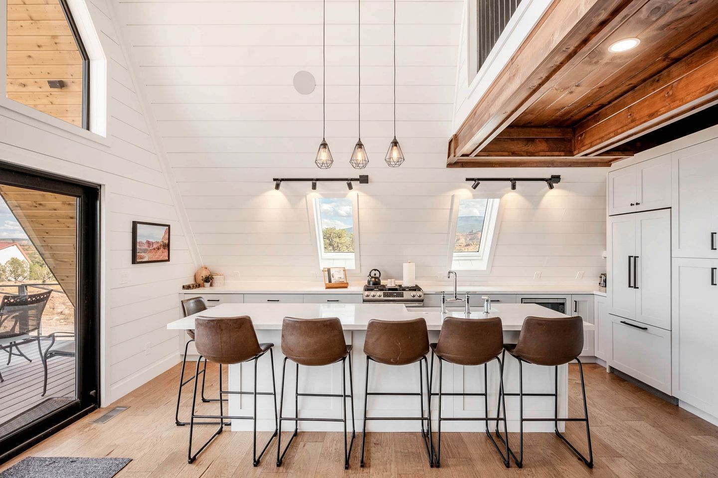 Una cucina moderna con isola centrale, sgabelli da bar, luci a sospensione e vista attraverso un lucernario.