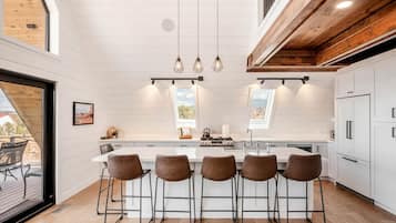 Una cucina moderna con isola centrale, sgabelli da bar, luci a sospensione e vista attraverso un lucernario.