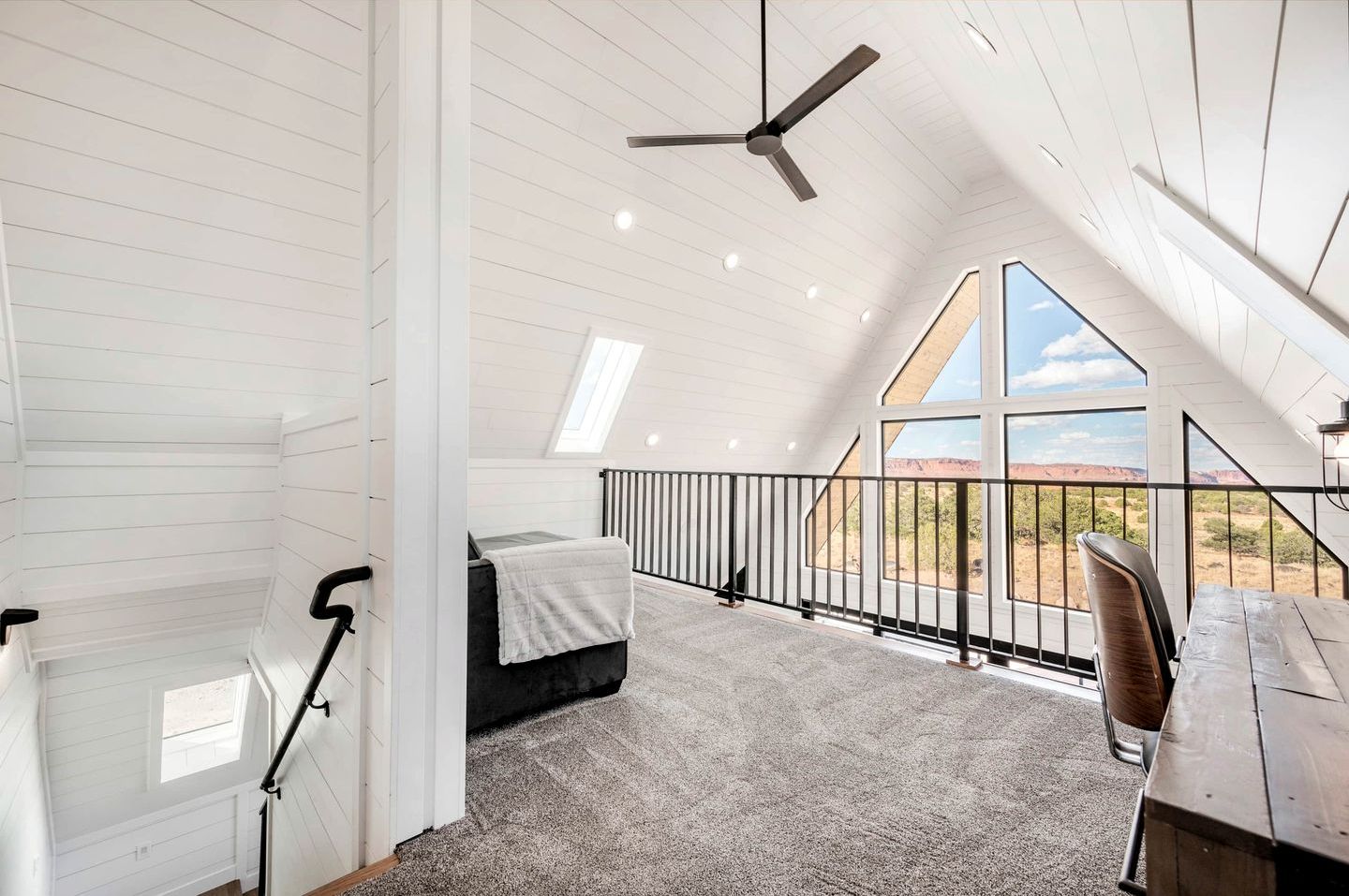 A bedroom with a bed, a desk, a chair, a ceiling fan, and a view of the outdoors.