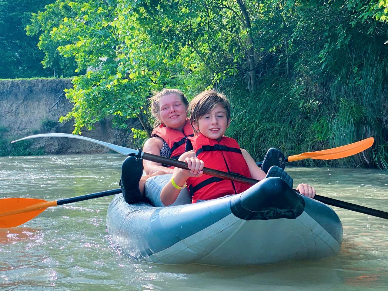 Two people in a raft on a river surrounded by greenery.