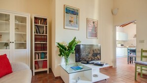 A living room with a TV, bookshelves, a glass coffee table, and a red pillow. - Apartments Florence - Canto dei Nelli (Firenze)