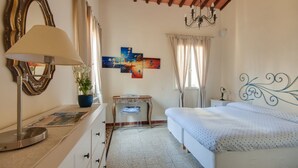 A bedroom with a bed, a desk, a chair, a lamp, a mirror, and artwork on the wall. - Apartments Florence - Canto dei Nelli (Firenze)