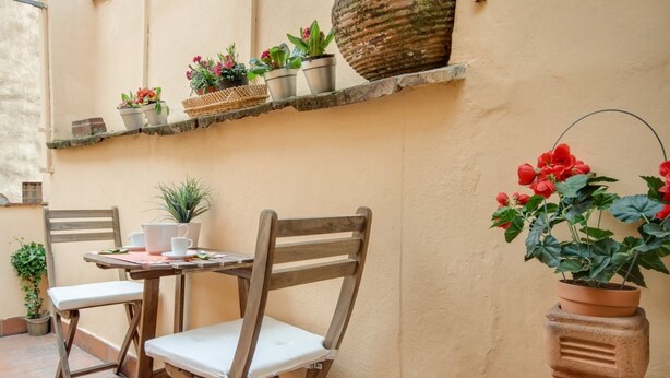 A wooden table and chairs set against a wall with potted plants and a stone shelf. - Apartments Florence - Canto dei Nelli (Firenze)