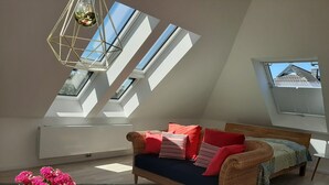 Ein Schlafzimmer im Loft-Stil mit schrägem Dach, einer Schlafcouch, einem Nachttisch, einer Topfpflanze und Dachfenstern.
