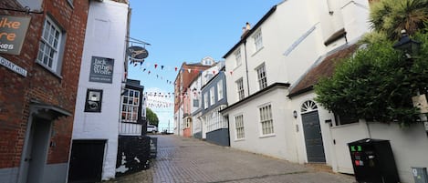 Rua de paralelepípedos com edifícios de ambos os lados, incluindo um pub chamado 'Jack & the Wolfe' com uma placa sobre a entrada.