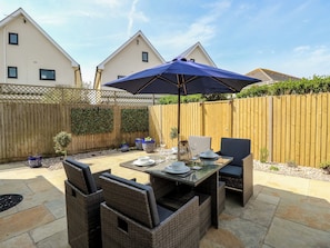 An outdoor patio with wicker furniture, a table set for dining, and a blue umbrella. - 50 Sea Road (Lymington)