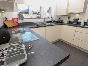 A modern kitchen with a granite countertop, a sink, and a window with a view of a fence and trees. - 50 Sea Road (Lymington)