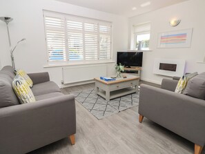 A modern living room with grey sofas, a coffee table, a TV, and a radiator. - 50 Sea Road (Lymington)