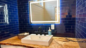 Un bagno con un lavandino bianco, piastrelle blu scuro e un piano in legno.
