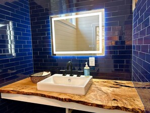 Un baño con un lavamanos blanco, azulejos azul oscuro y una encimera de madera.