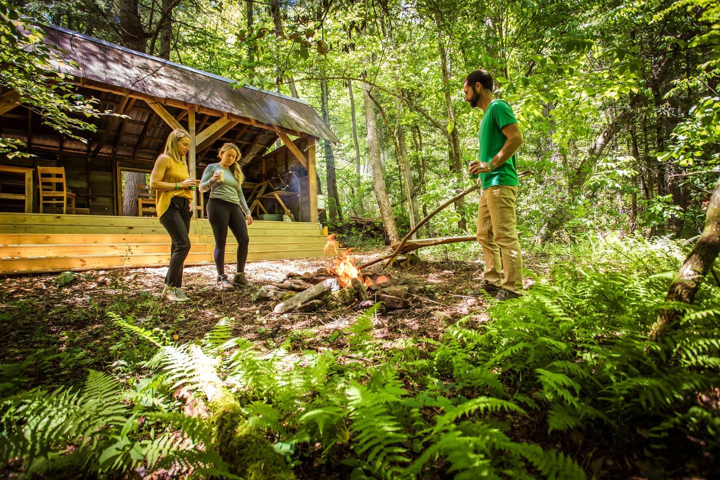 A rustic wooden cabin with a thatched roof, surrounded by dense forest.