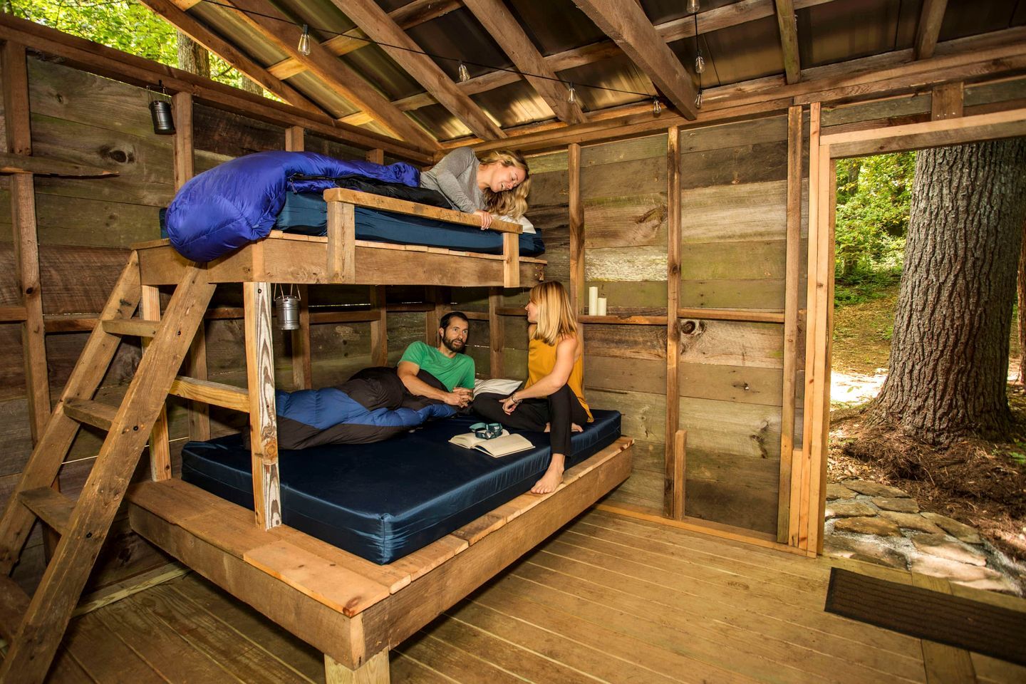 A rustic wooden cabin with bunk beds, a ladder, and a small table with a book.