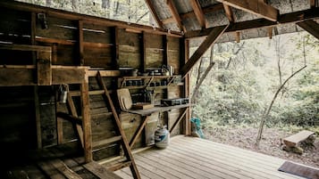Una cabaña rústica de madera con un balcón de madera, estantes con utensilios de cocina y vista al bosque.