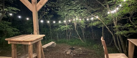 En träaltan med ett bord och stolar, omgiven av en stenmur och dekorerad med ljusslingor.