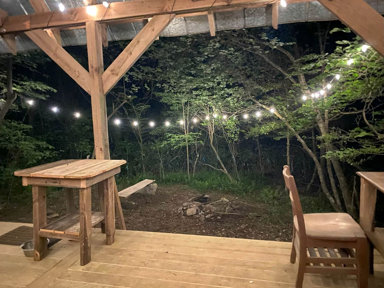 A wooden deck with a table and chairs, surrounded by a stone wall and string lights.