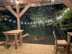 Eine Holzterrasse mit Tisch und Stühlen, umgeben von einer Steinmauer und Lichterketten.