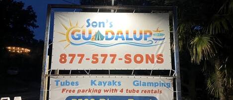 A sign for Son's GUDA LUPS with contact number 877-577-SONS, offering tubes, kayaks, and glamping with free parking and 4 tube rentals.
