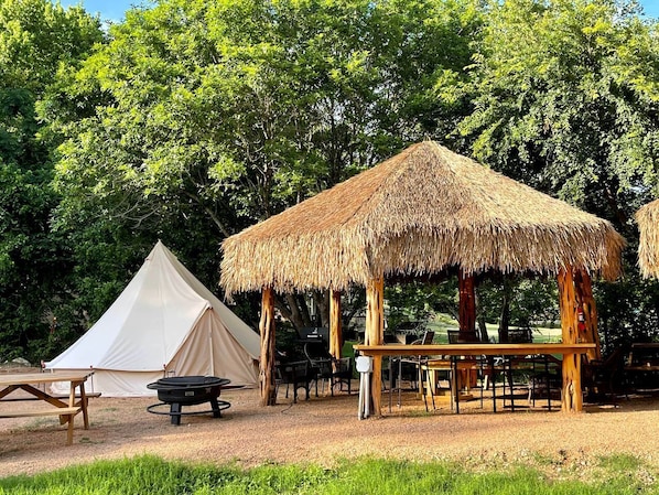 A campsite with a tent, a wooden table, and a thatched structure.