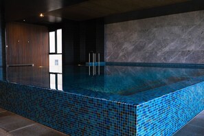 A modern indoor swimming pool with a blue-tiled edge, a wooden panel wall, and a marble wall. - Southbank Urban Haven! (Southbank)