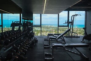 A gym with weight machines and dumbbells, large windows with a city and ocean view. - Southbank Urban Haven! (Southbank)
