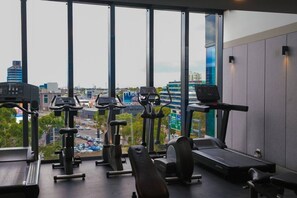 Ein Fitnessstudio mit unterschiedlichen Trainingsgeräten, großen Fenstern und Blick auf die Stadt.