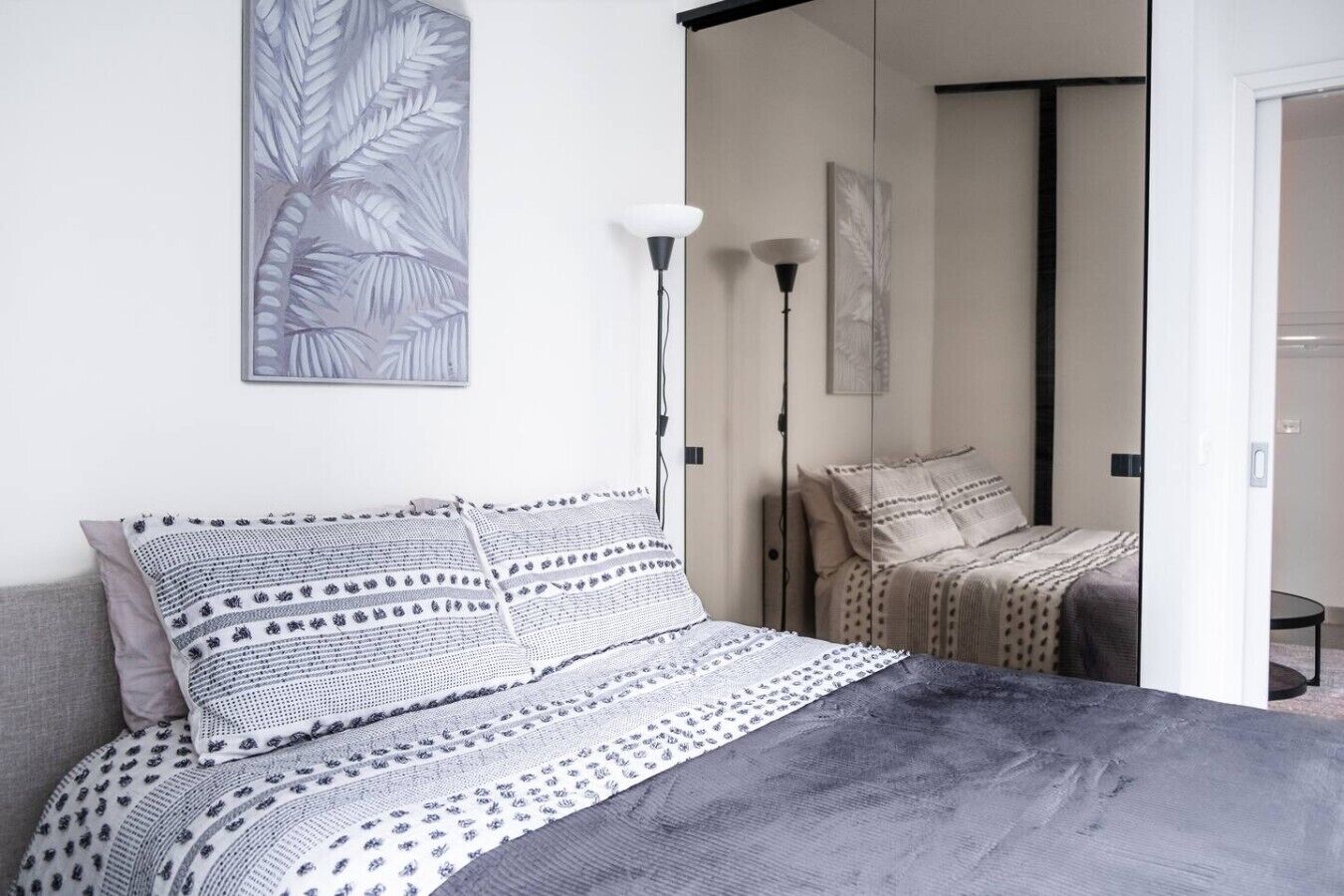 Ein Schlafzimmer mit einem Bett, Kissen, einer Lampe und einer Tür zu einem anderen Raum.