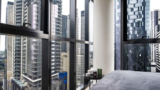 Ein Hotelzimmer in einem Hochhaus mit großen Fenstern, einem Bett und einem kleinen Tisch mit Tasse und Buch.