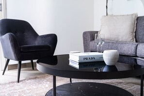 Ein modernes Wohnzimmer mit einem schwarzen Sessel, einem grauen Sofa, einem schwarzen Couchtisch mit Büchern und einer dekorativen Schale, sowie einem weißen Kissen auf dem Sofa.