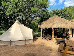 A tent, a thatched structure, and picnic tables in a campsite.
