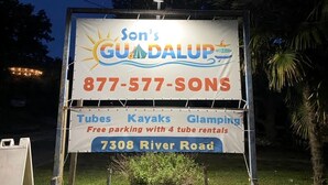 Schild für Son's GUDA LUPS mit der Kontaktnummer 877-577-SONS, das Schlauchboote, Kajaks und Glamping mit kostenlosem Parkplatz und 4 Schlauchbootverleihungen anbietet.