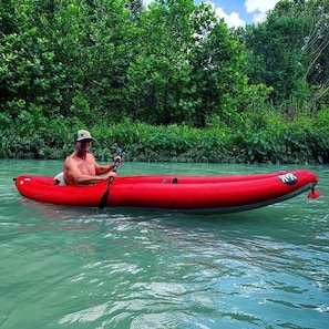 A man in a red kayak on a river surrounded by dense greenery.