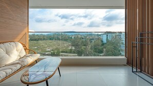 Un balcón con vista a un paisaje urbano, un sofá de mimbre y una mesa de vidrio.