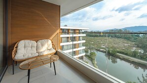 Un balcón con un sofá de mimbre, vista a un río y un edificio moderno al fondo.