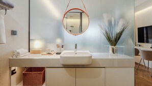 Un baño moderno con un lavamanos blanco, un espejo redondo y una cesta de mimbre.