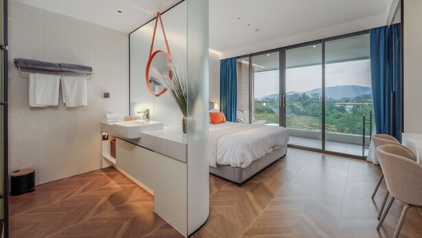 Habitación de hotel moderna con una cama grande, baño con tocador y un balcón con vistas.