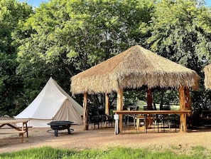 Ein Campingplatz mit Zelt, einer Holzhütte mit einem Reetdach und einem Picknicktisch.