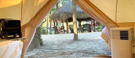 A tent with a table and an air conditioning unit inside, and a thatched structure outside.