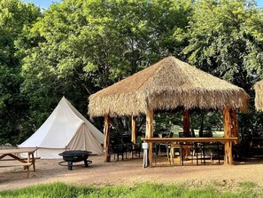 Ein Campingplatz mit Zelt, einer Holzhütte mit einem Reetdach und einem Picknicktisch.