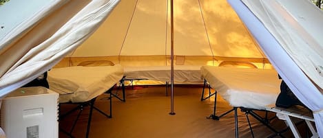 A tent with two beds, a central pole, and a white cooler.
