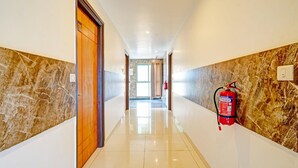 A hallway with marble walls, a fire extinguisher mounted on the wall, and a door labeled '106'. - Deluxe Kaveri Road Mysore Nisarga (Mysore)