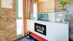 A reception desk with a 'HOTELO' sign, a potted plant, and a window with curtains. - Deluxe Kaveri Road Mysore Nisarga (Mysore)