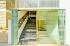A staircase leading to a building entrance with a glass door and a brick wall. - Deluxe Kaveri Road Mysore Nisarga (Mysore)