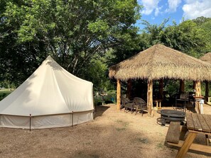 A tent, a thatched structure, and picnic tables in a campsite.