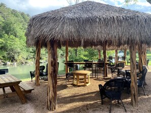 A thatched-roof pavilion with outdoor seating and a view of a lake.